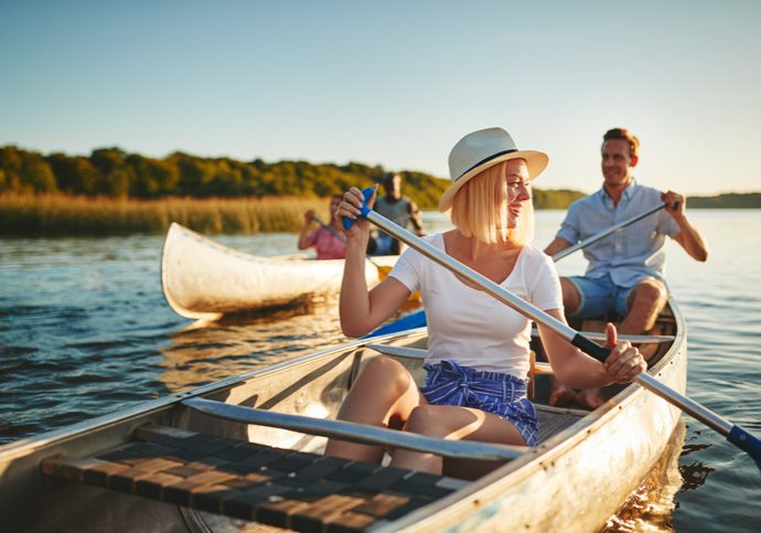 Young woman laughing while paddling a canoe on a lake with her boyfriend and another couple on a sunny summer afternoon